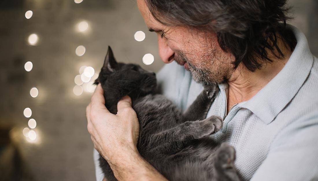 Homme souriant à un chat gris qu'il tient