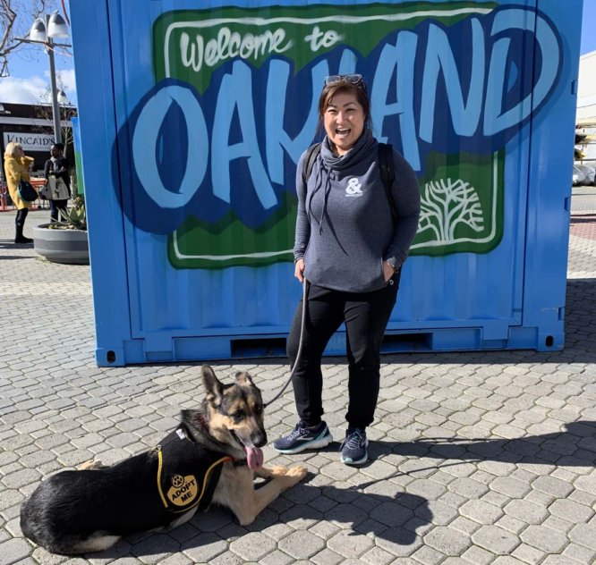 Dog and dog walker by "Welcome to Oakland" sign.