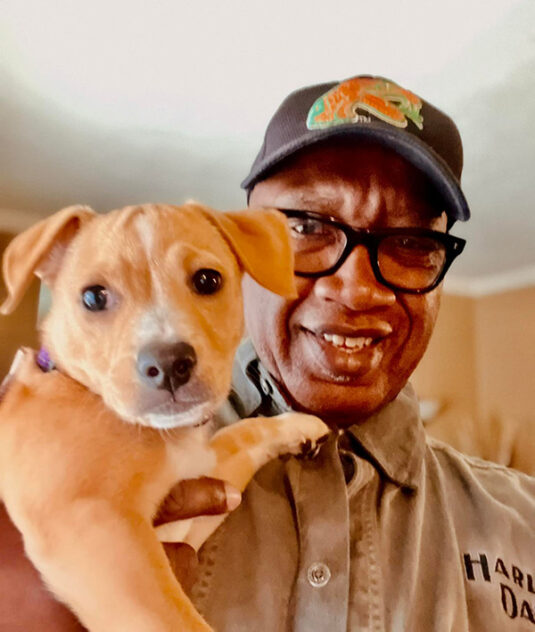 Mayor Welch is smiling and holding up a puppy.