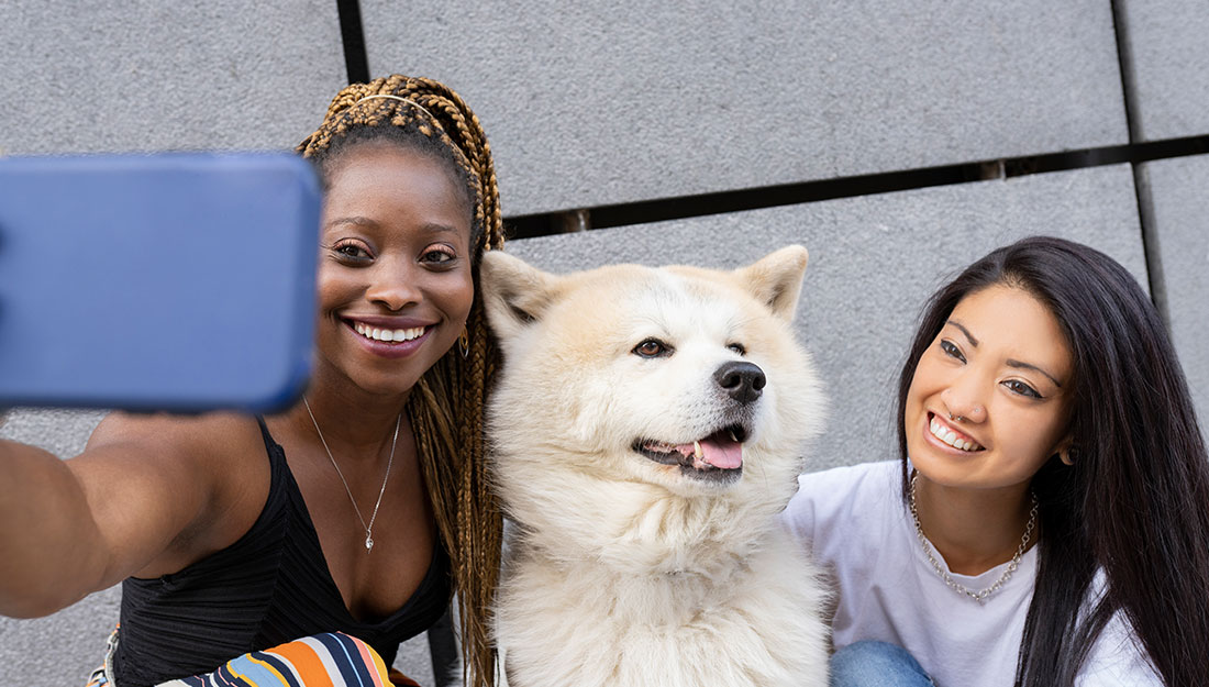 Two women pose for a selfie with a cute white dog between them