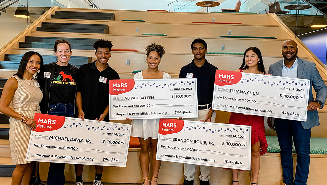 Scholarship recipients pose holding giant commemorative checks, along with representatives from Mars Petcare.