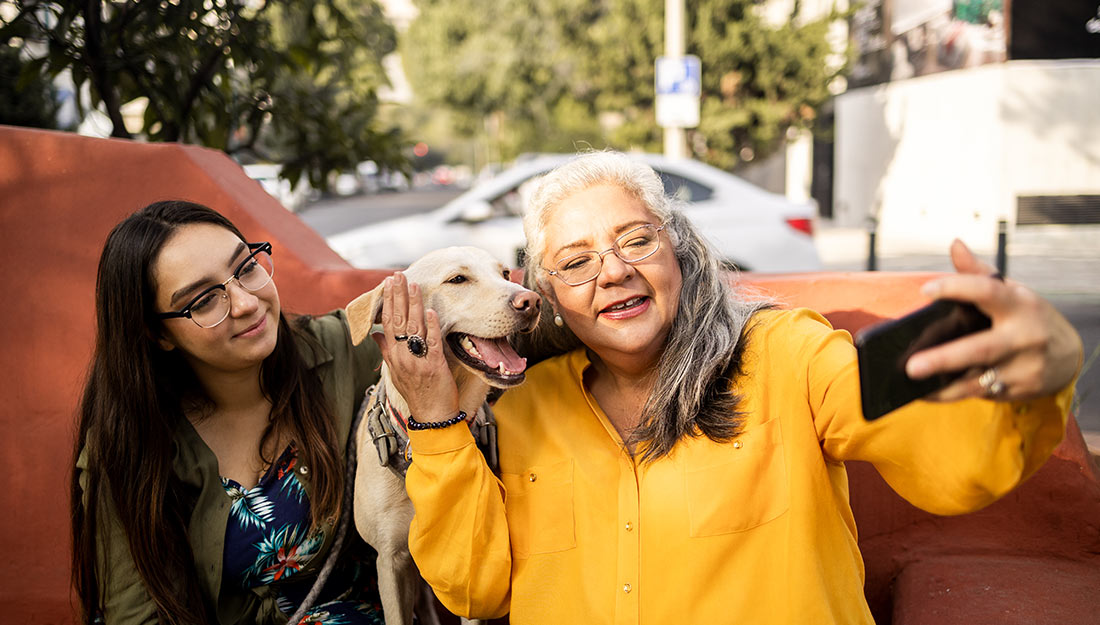Une famille est assise sur un banc extérieur et pose pour un selfie avec son chien heureux.