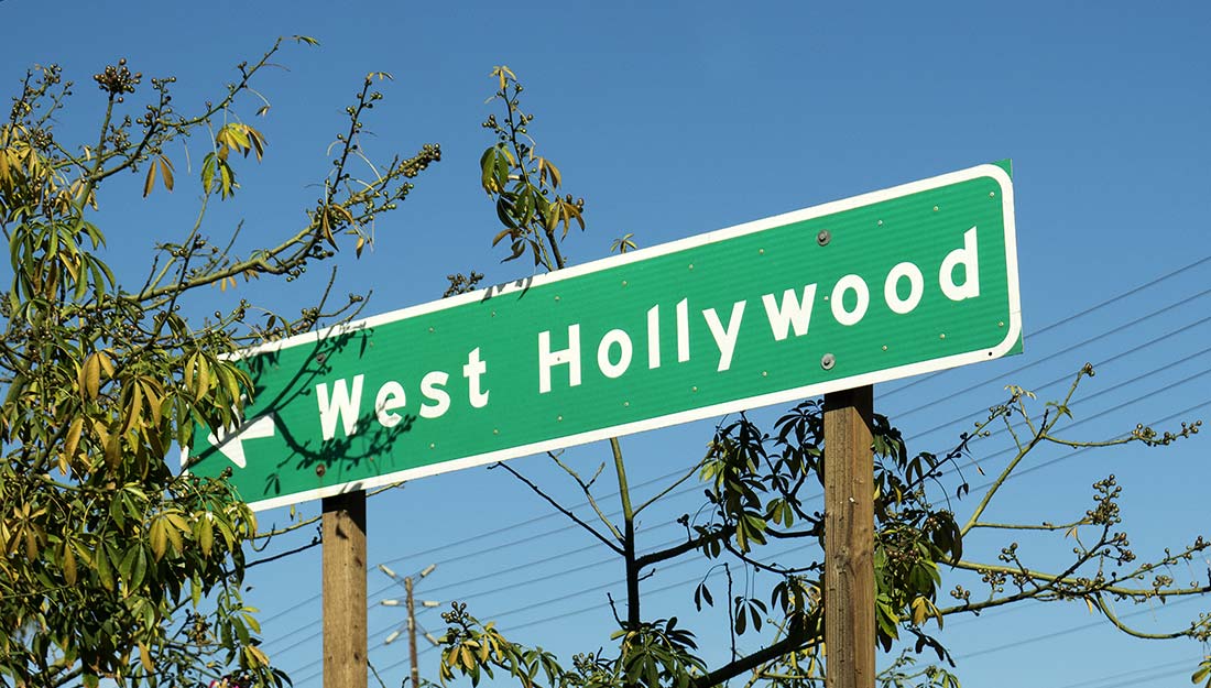 Un panneau de rue qui dit "West Hollywood" contre un ciel bleu.