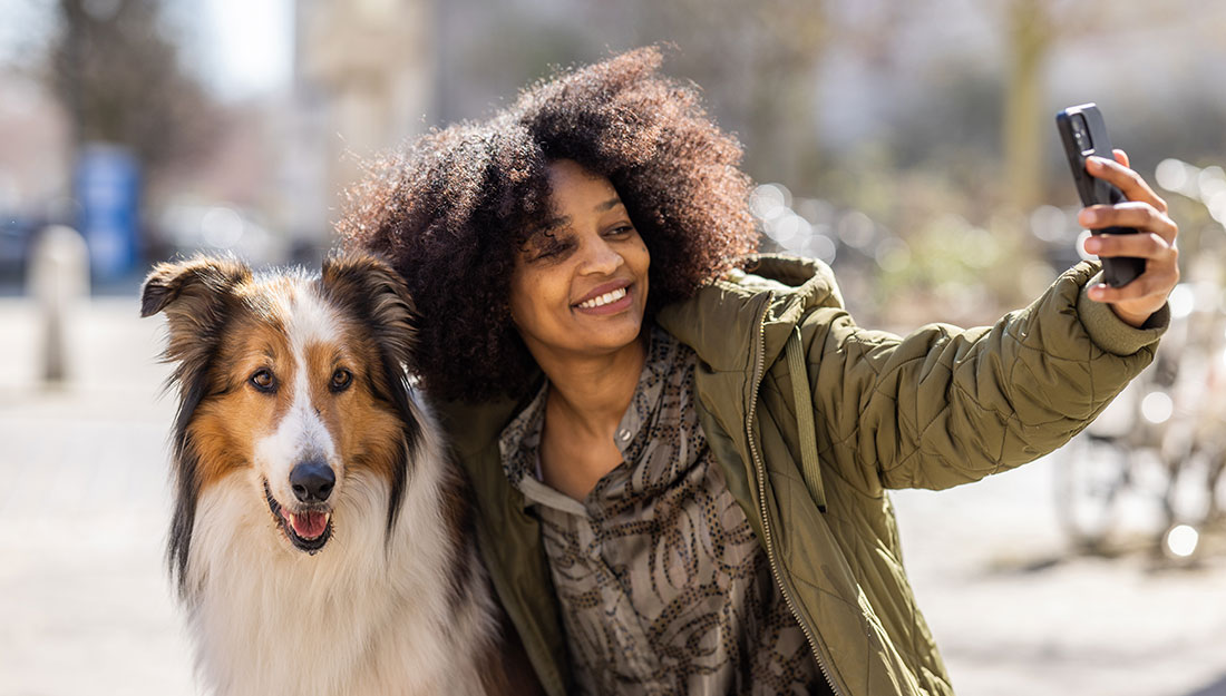 A woman poses for a selfie with a dog by her side.